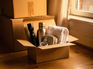 Open verhuisdoos met zaklamp, waterfles, oplader, toilettas en handdoek op houten vloer naast dichte dozen in Amsterdam appartement.